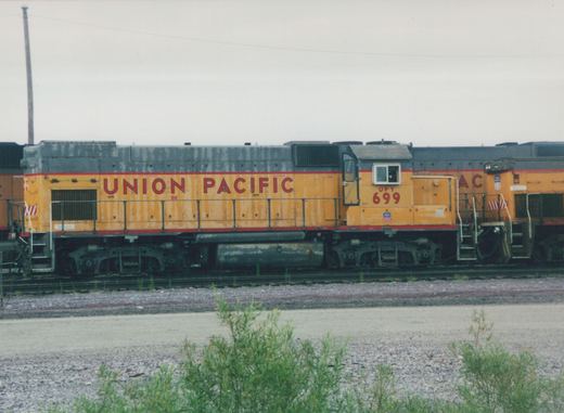 A side view of a yellow and red Union Pacific diesel locomotive numbered 699, parked in a gravel yard under an overcast sky.