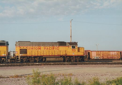 A side view of a yellow and red Union Pacific diesel locomotive, number 712, at a rail yard with a freight car behind it under a clear sky.