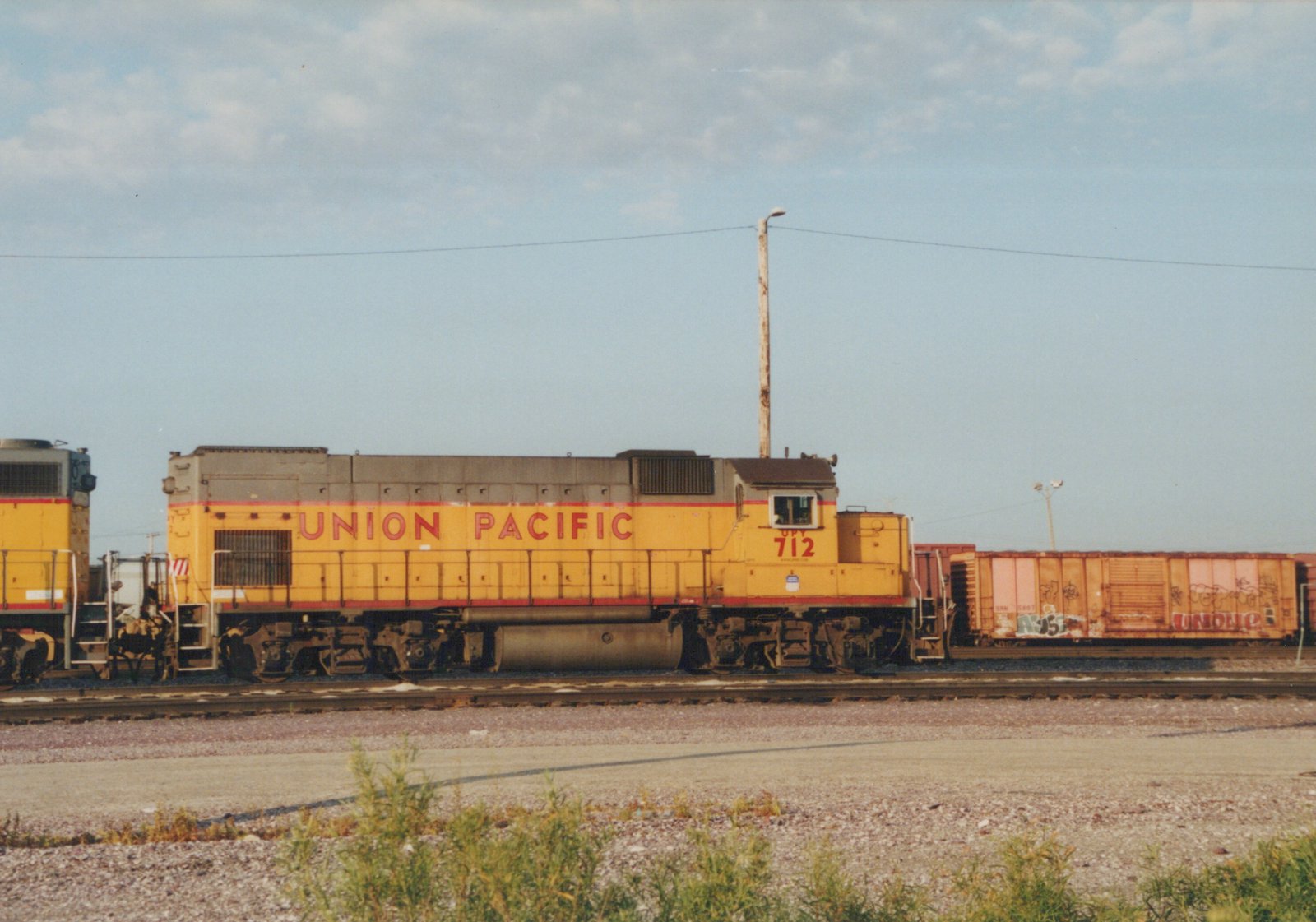A side view of a yellow and red Union Pacific diesel locomotive, number 712, at a rail yard with a freight car behind it under a clear sky.