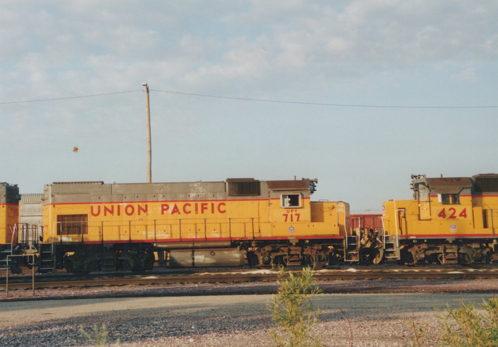 A side view of two yellow Union Pacific diesel locomotives, numbers 717 and 424, stationed on parallel tracks in a gravel yard with a cloudy sky above.