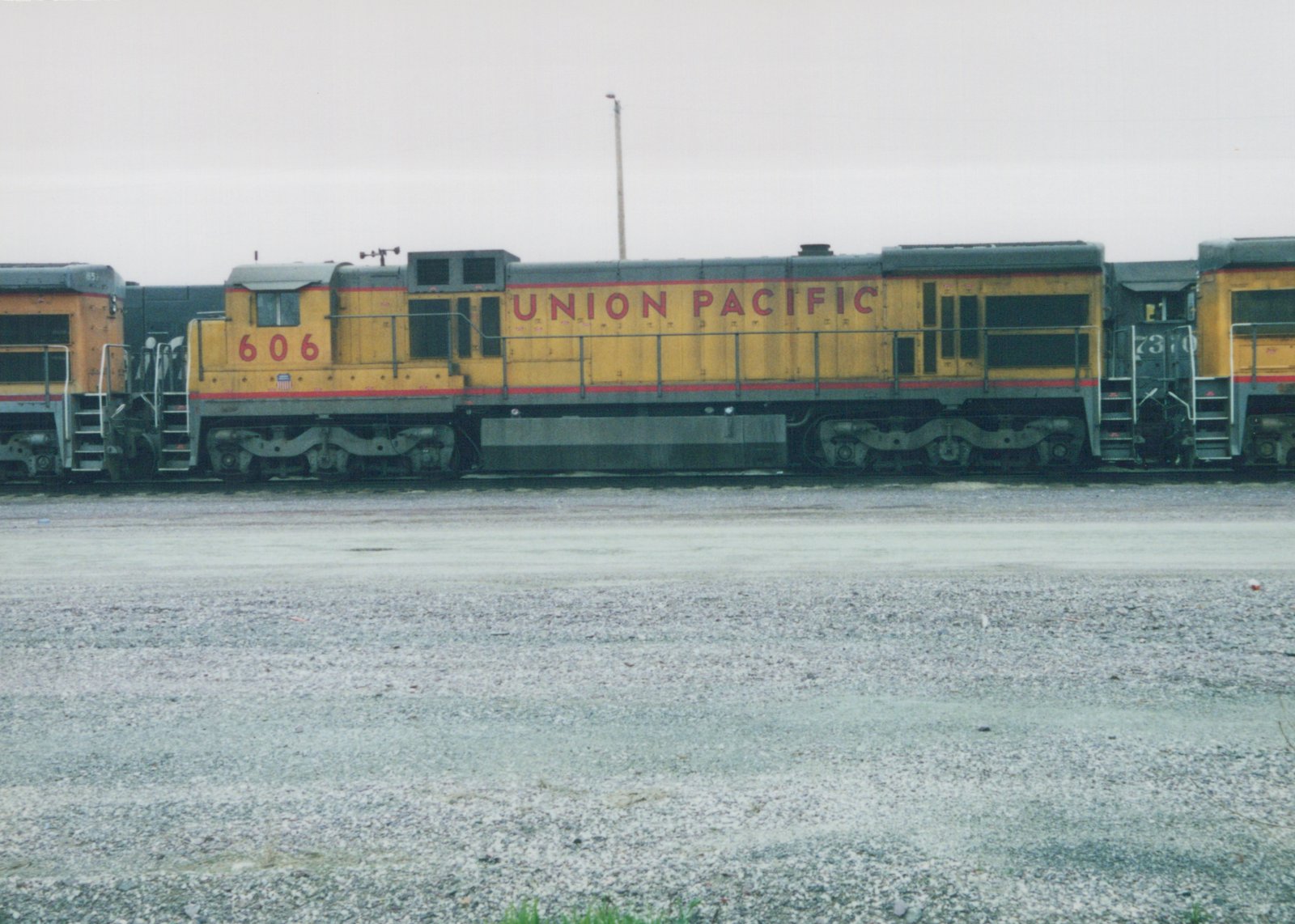 Side view of a yellow and gray Union Pacific diesel locomotive, number 606, parked in a gravel yard with another locomotive behind it, both bearing the 'Union Pacific' name in red lettering.
