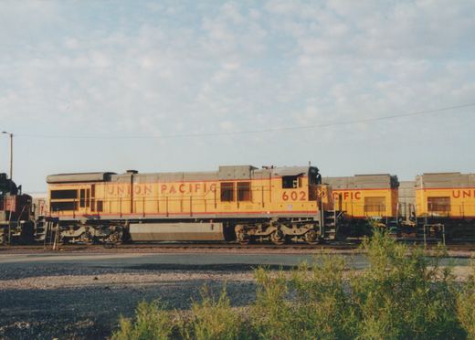 A side view of a Union Pacific diesel locomotive, number 602, painted in yellow and gray, parked in a rail yard with two similar locomotives behind it.