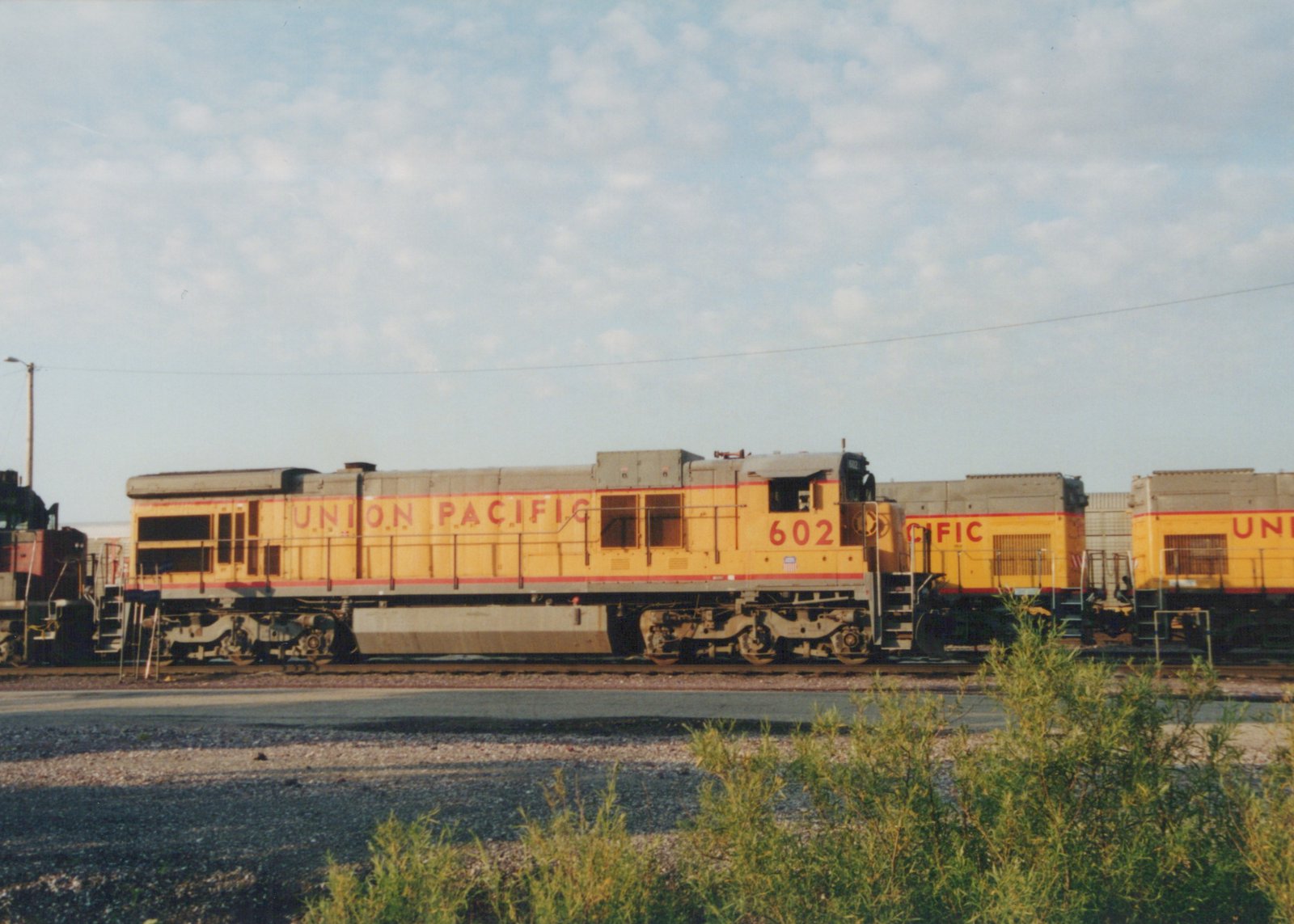 A side view of a Union Pacific diesel locomotive, number 602, painted in yellow and gray, parked in a rail yard with two similar locomotives behind it.