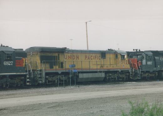 A row of Union Pacific diesel locomotives, including number 502, sit on parallel tracks in a gravel yard with a cloudy sky above.