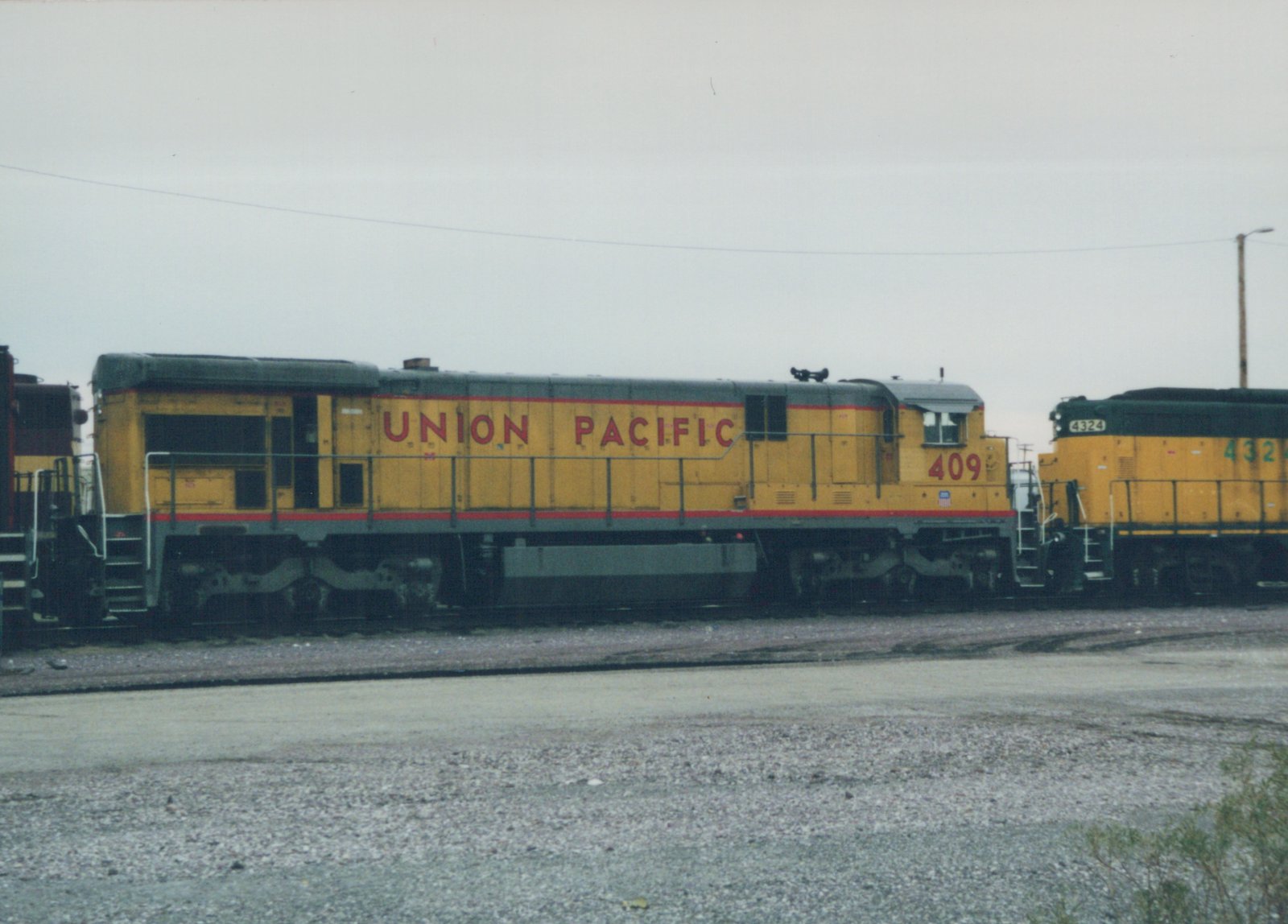 Two Union Pacific diesel locomotives, numbers 409 and 4324, are parked side by side in a gravel-covered rail yard under an overcast sky.