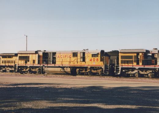 Side view of a yellow Union Pacific diesel locomotive with red stripes and 'PACIFIC' lettering, numbered 408, parked in a gravel yard next to another similar locomotive under a clear sky.