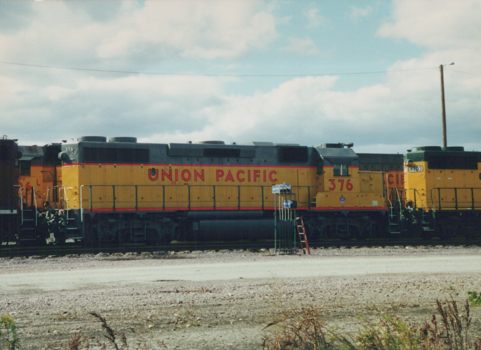 Two yellow and gray Union Pacific diesel locomotives, numbered 376 and 4703, are parked side-by-side on railroad tracks in a gravel yard under a cloudy sky.