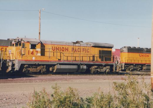 Two yellow Union Pacific diesel locomotives, numbered 147 and 2973, are parked on parallel tracks in a gravel yard under a clear blue sky.