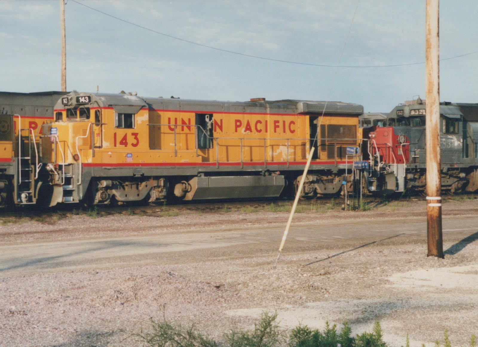 A side view of a yellow and red Union Pacific diesel locomotive, number 143, in a gravel yard with another locomotive behind it.