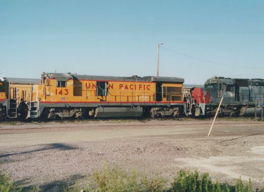Side view of a yellow Union Pacific locomotive 143 in a rail yard, with a dark gray Southern Railway locomotive 832 behind it on a clear summer day.