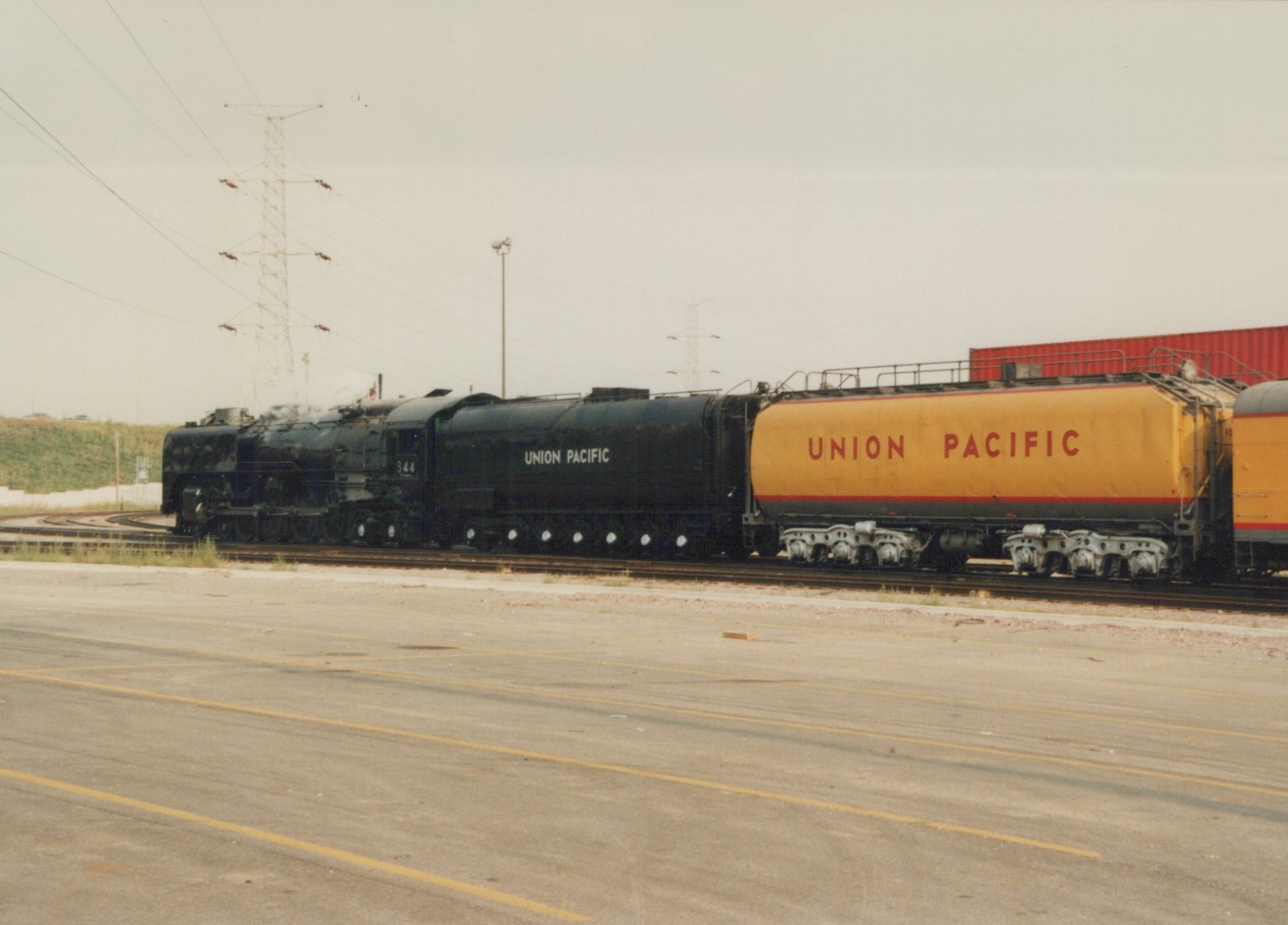 A large black Union Pacific steam locomotive numbered 344 stands on tracks in a yard, with a yellow tanker car behind it.