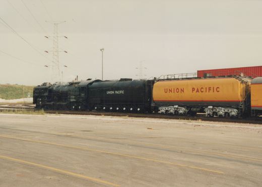 A large black Union Pacific steam locomotive numbered 344 stands on tracks in a yard, with a yellow tanker car behind it.