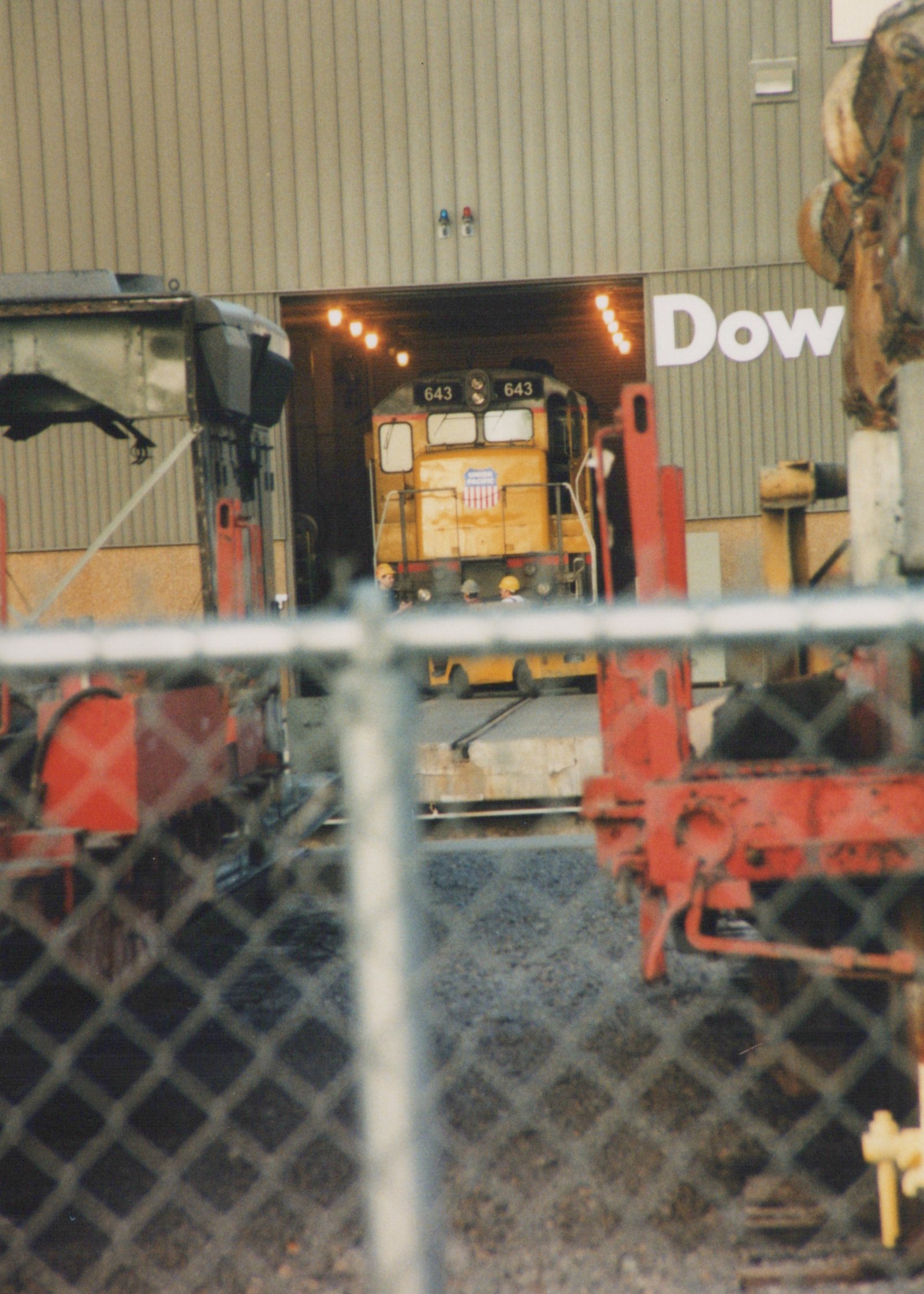 Union Pacific locomotive number 643, a GP9 model, is parked in a rail yard with a red piece of equipment in front and a Dow Chemical building behind it.