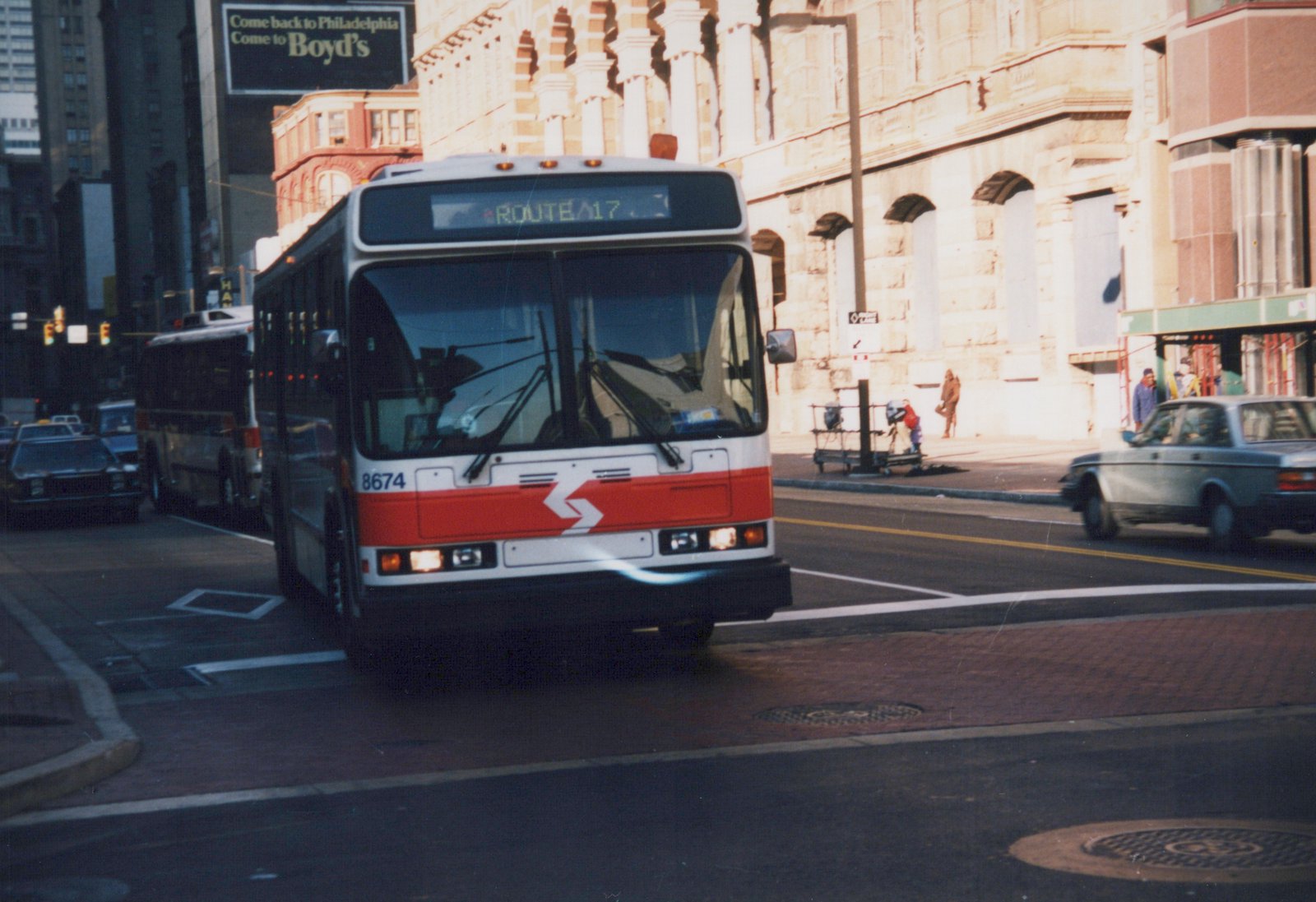 A white and red SEPTA bus number 8674 on Route 17 is turning on a city street with buildings and other vehicles in the background.