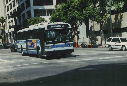 A white and blue city bus with the destination '10 Santa Monica via Freeway' is turning on a city street, surrounded by trees and buildings. The bus number is 4820 and it has a 'Hercules' advertisement on its side.