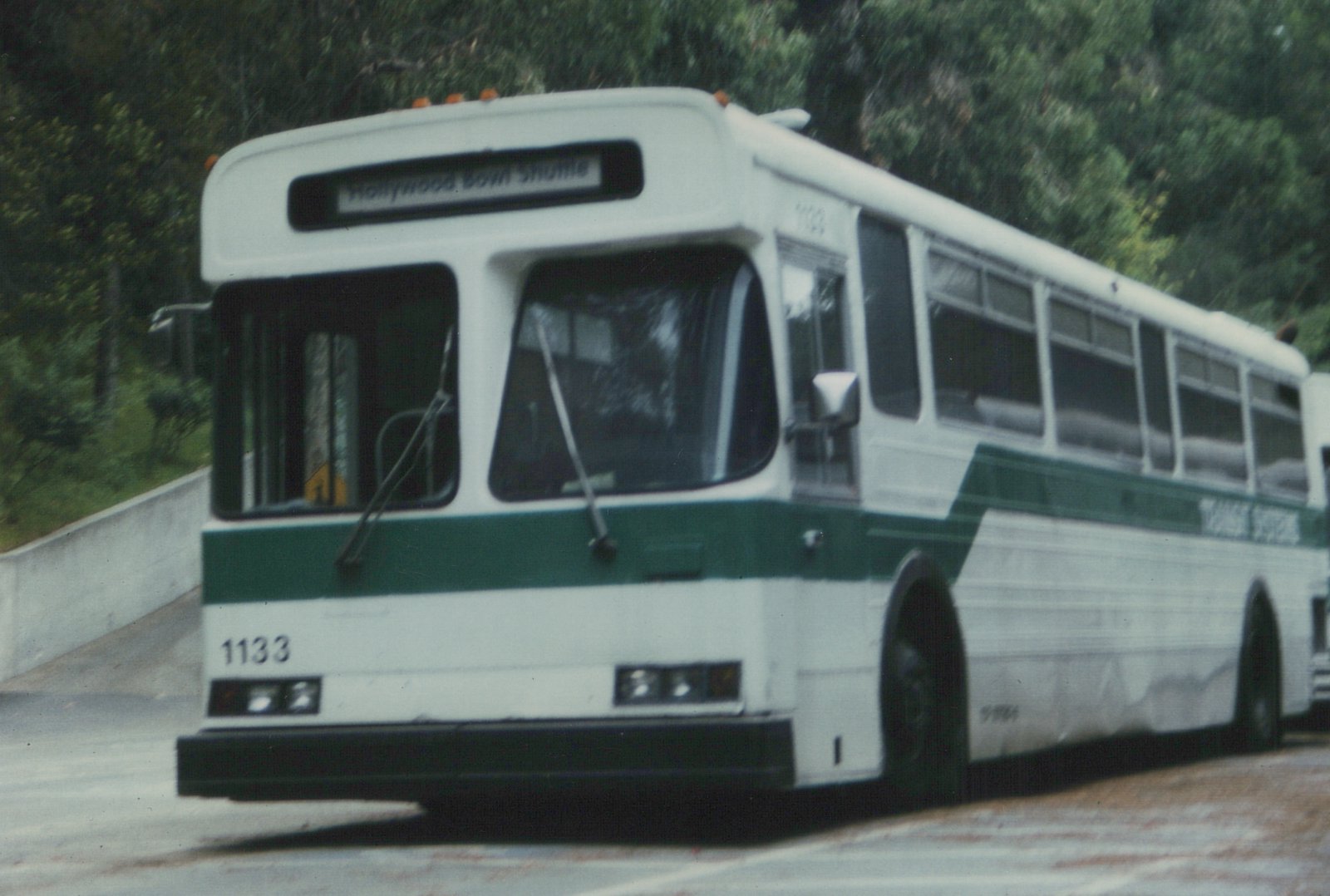A white and green transit bus with the destination sign 'Hollywood Bowl Shuttle' and the fleet number 1133, parked on a street with trees in the background.