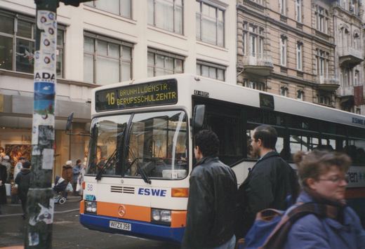 A Mercedes-Benz O405 bus operated by ESWE, numbered 58, is stopped on a city street with people walking by and a destination sign showing route 16 to Brunhildenstr. Berufsschulzentr.