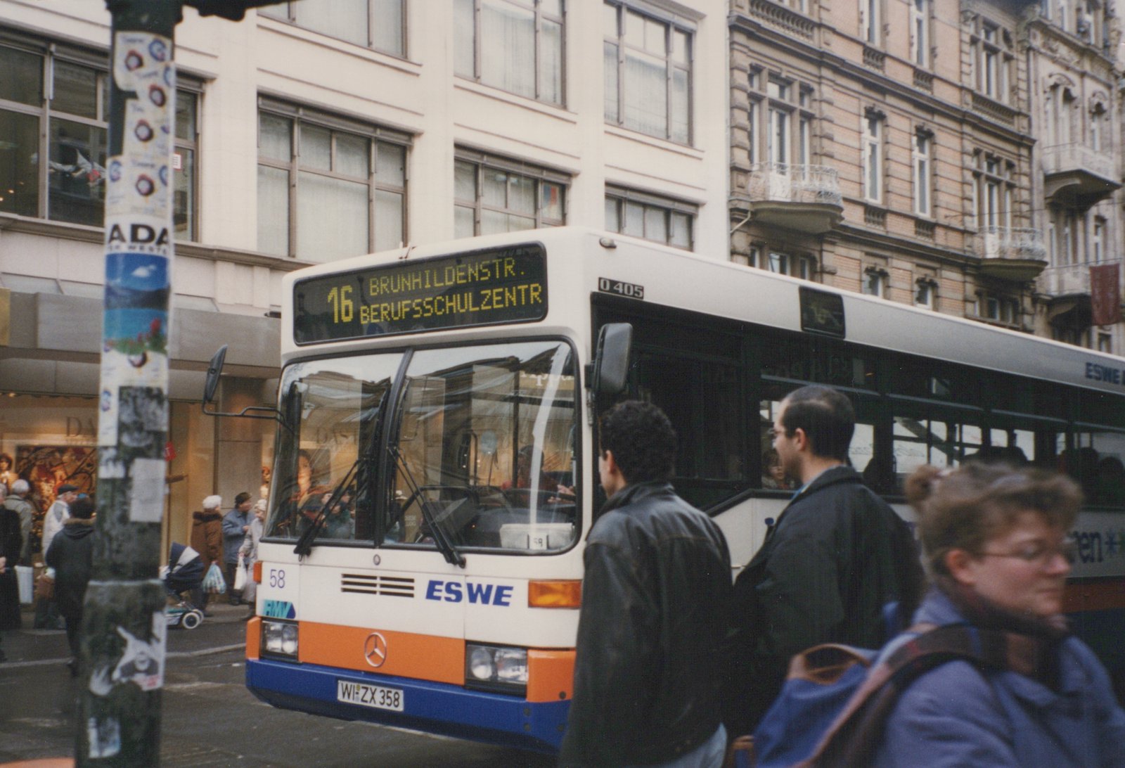 A Mercedes-Benz O405 bus operated by ESWE, numbered 58, is stopped on a city street with people walking by and a destination sign showing route 16 to Brunhildenstr. Berufsschulzentr.