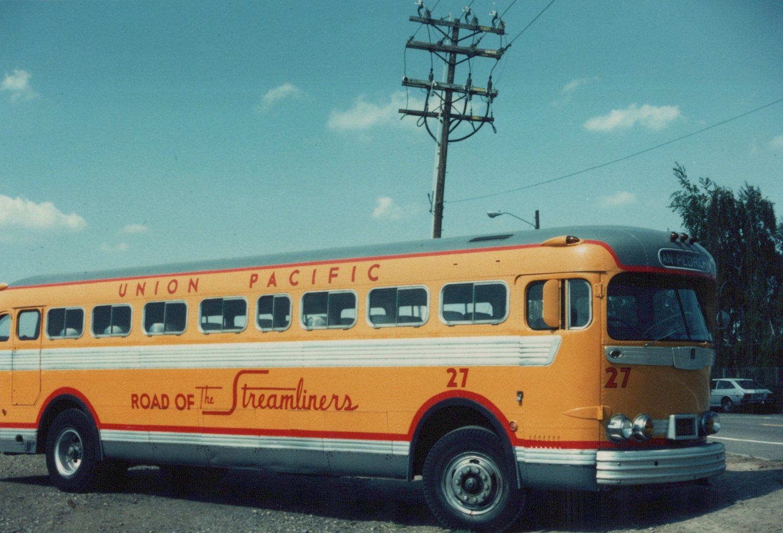 A vintage orange and grey Union Pacific bus, numbered 27, with 'Road of The Streamliners' written on its side, parked outdoors with a clear blue sky above.
