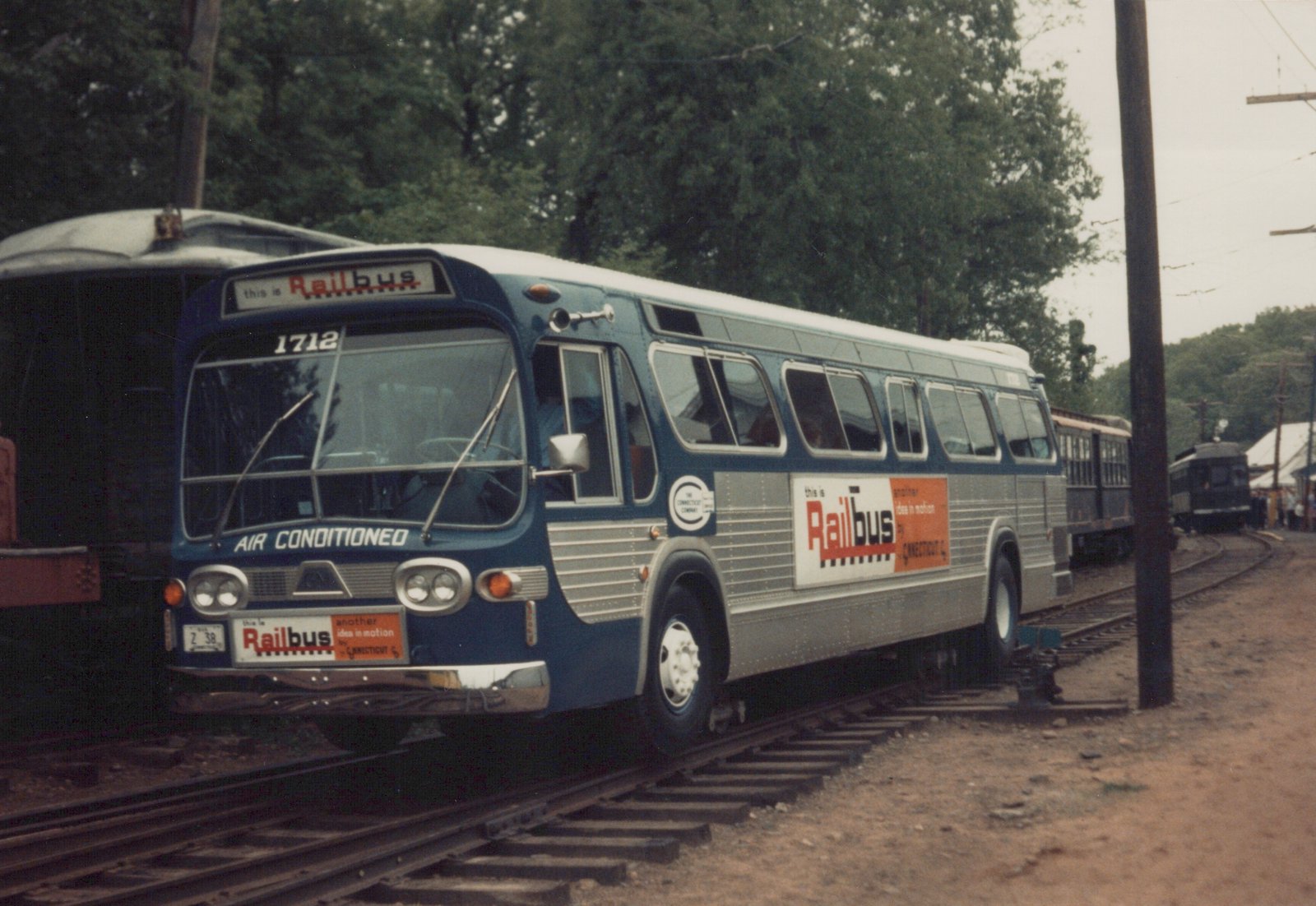 A blue and silver motor bus labeled 'Railbus' is positioned on railroad tracks, with old interurban cars visible behind it.