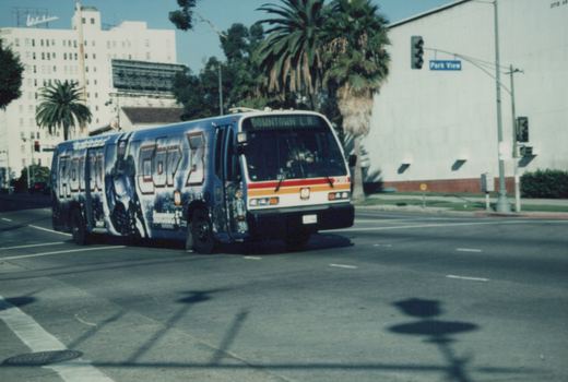 A blue and white bus with a 'RoboCop 3' ad on its side drives down a street lined with palm trees, with a 'Park View' street sign visible.