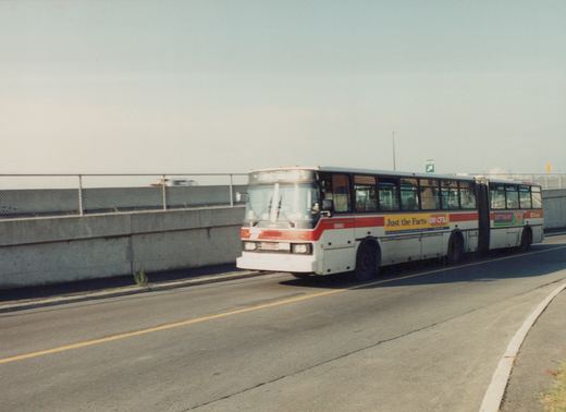 A white and red articulated bus with the number 8950 on its side drives on a highway with a concrete barrier and a chain-link fence in the background.