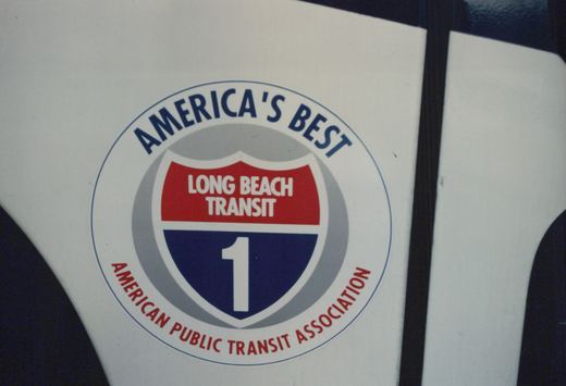 Close-up of a circular decal on a white surface. The decal has a blue border with 'AMERICA'S BEST' on top and 'AMERICAN PUBLIC TRANSIT ASSOCIATION' on the bottom. In the center is a shield with 'LONG BEACH TRANSIT' in white text on a red background and a large white number '1' on a blue background.