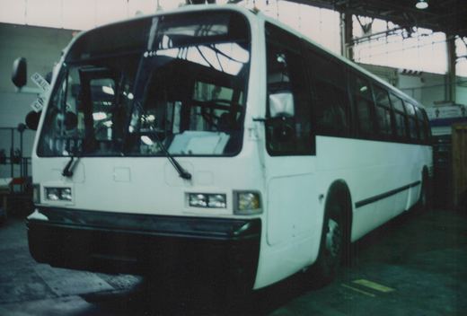A front three-quarter view of a white Pace bus with the number 7 on its windshield, parked inside a large garage with high windows.