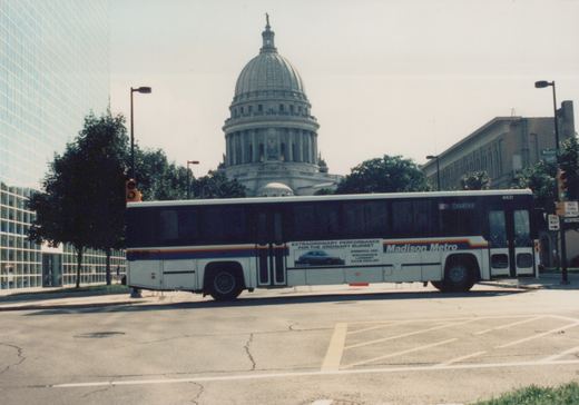 A white Madison Metro bus with fleet number 4431 is parked on a city street, with the Wisconsin State Capitol visible in the background under an overcast sky.