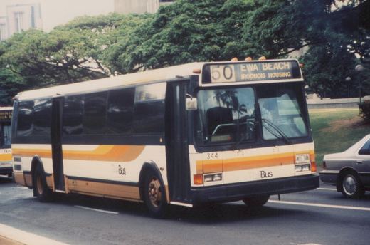 A white and orange bus with the number 344 and destination Ewa Beach is driving on a city street with trees and a car nearby.