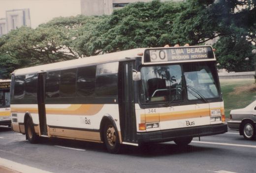 A white and yellow motor bus with 'The Bus' lettering and the number 344, displaying route 50 to Ewa Beach, is driving on a street with trees and buildings in the background.