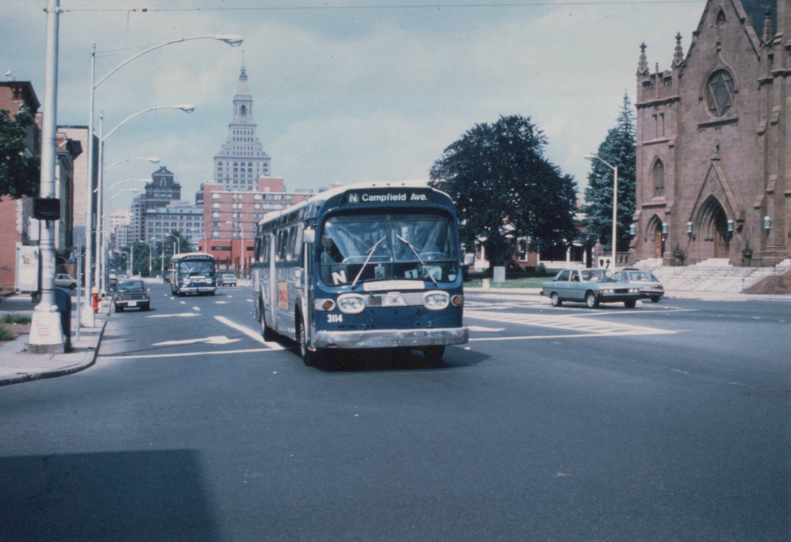 A blue and white CTA bus numbered 3114 on a city street, heading toward a destination sign reading 'N Campfield Ave.', with a church on the right and another bus behind.