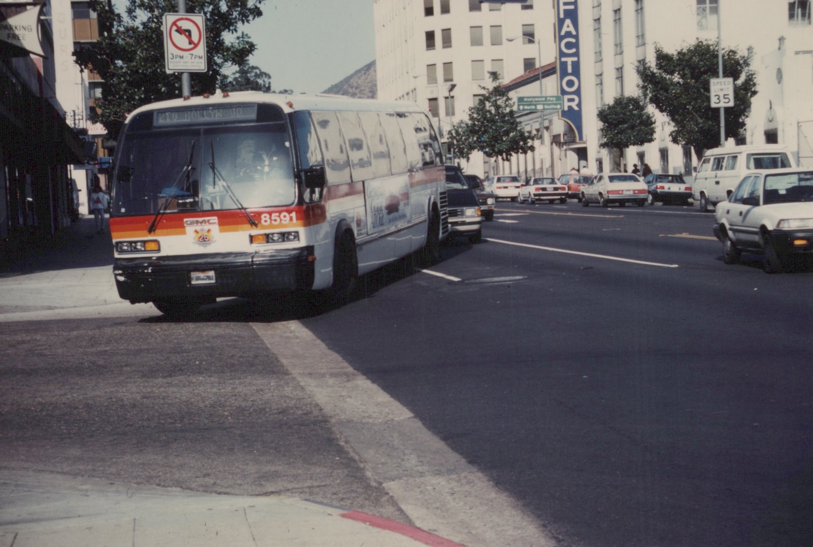 A white and orange motor bus with the number 8591 on its front drives down a city street with other cars and buildings in the background.