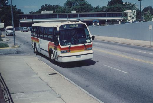 A white bus with red and yellow stripes, marked CAT and number 1206, is driving on a city street with a United States Post Office building in the background.