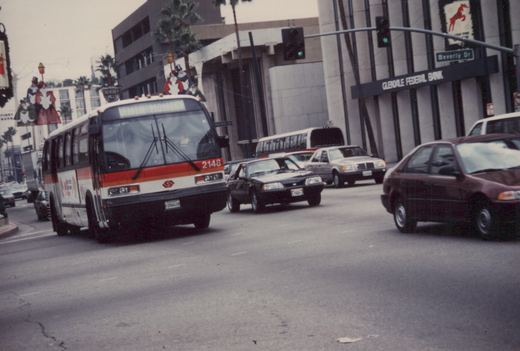 A white, orange, and red Southern California Rapid Transit District bus, number 2148, is driving down a city street with other cars and a 'Beverly Dr' street sign visible.