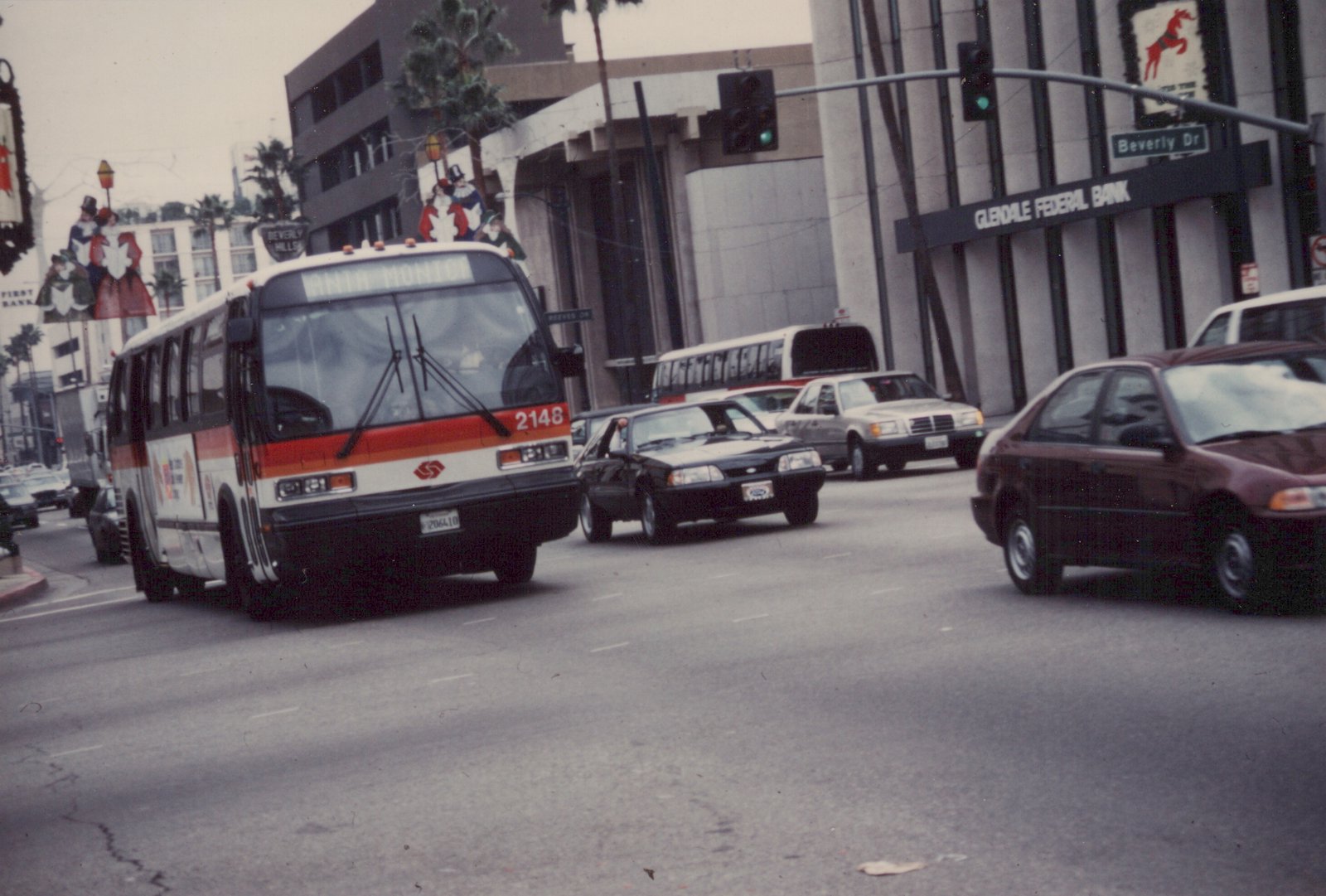 A white, orange, and red Southern California Rapid Transit District bus, number 2148, is driving down a city street with other cars and a 'Beverly Dr' street sign visible.