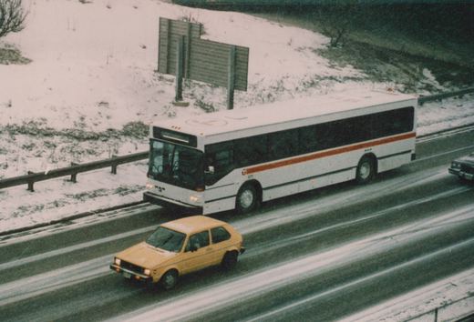 A white and red Regional Transportation Authority bus, fleet number 1211, drives on a snow-covered expressway, with a yellow car in an adjacent lane.