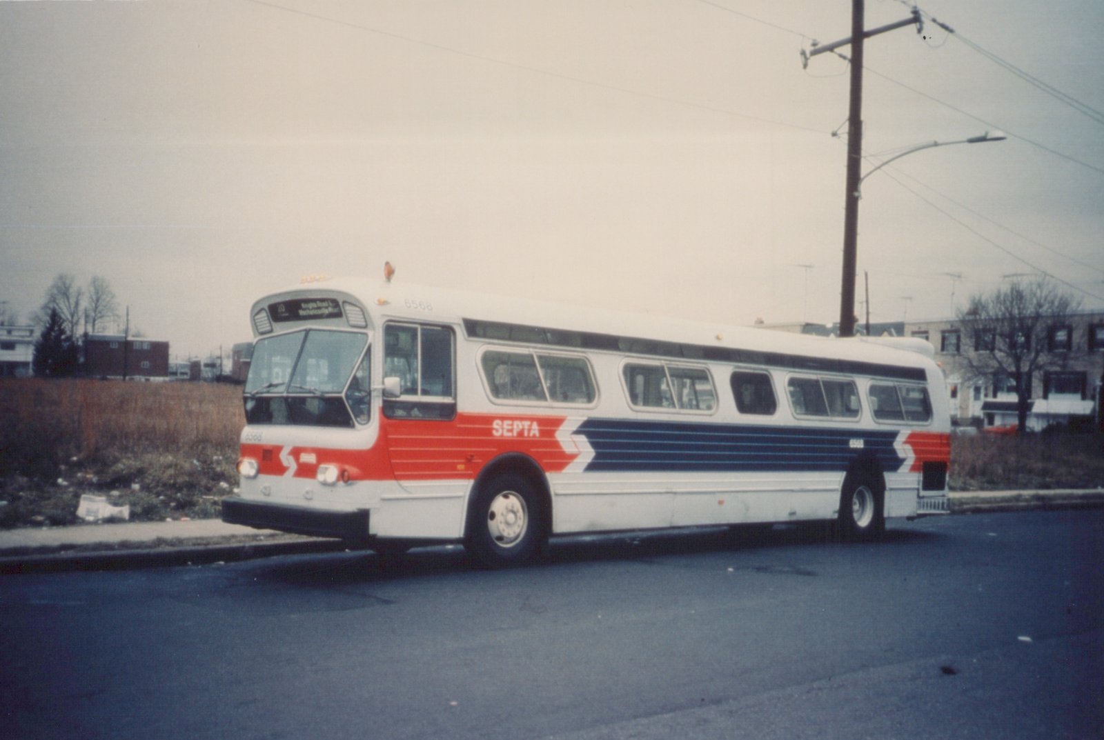 A white, red and blue SEPTA bus numbered 6568 is parked on a street with bare trees and buildings in the background under a grey sky.
