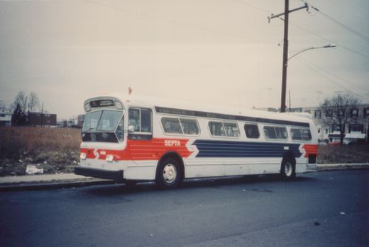 A white, red and blue SEPTA bus numbered 6568 is parked on a street with bare trees and buildings in the background under a grey sky.