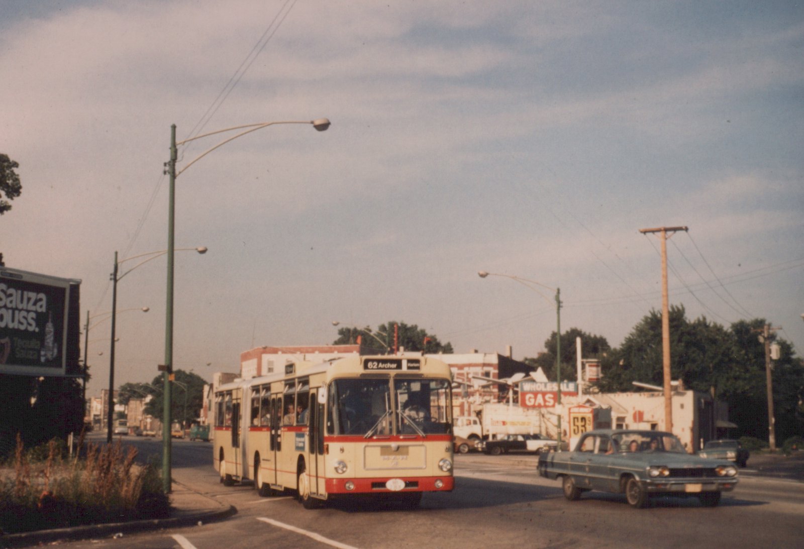 A cream and red Chicago Transit Authority bus on a city street with a 1960s car, a gas station, and a billboard in the background.