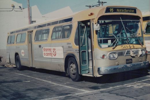 A yellow and silver RTD bus numbered 5044 is parked in a yard, featuring a Salvation Army ad reading 'sharing is caring' and a destination sign showing '95 Not in Service'.