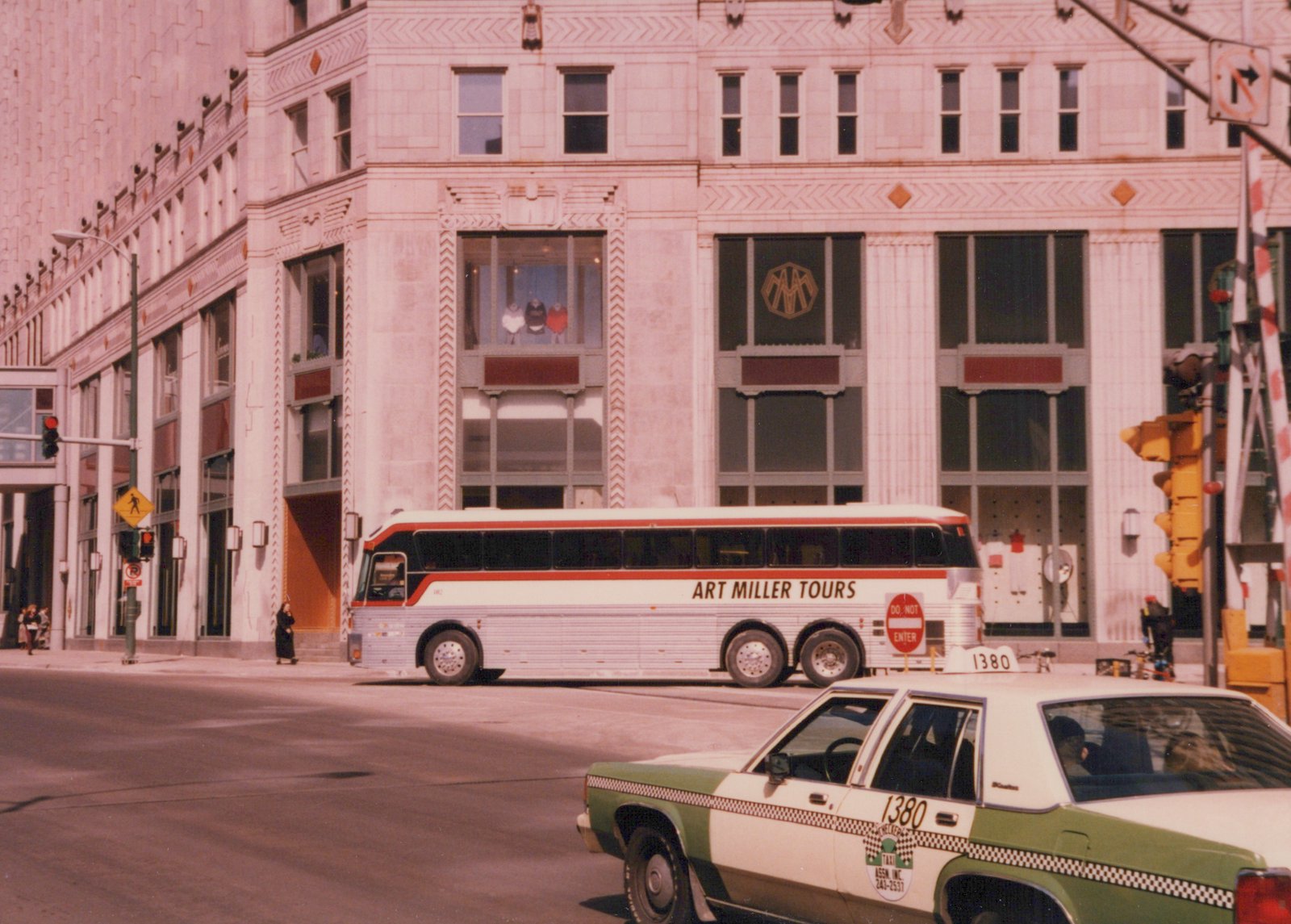 A white and red motor bus labeled 'Art Miller Tours' and numbered 1380 is parked on a city street beside a green and white Checker taxi. A large Art Deco-style building stands behind them.