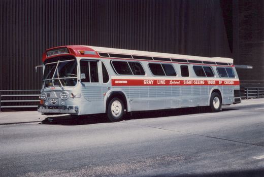 A silver and red Gray Line tour bus with the number 506, parked on a city street in front of a dark building.