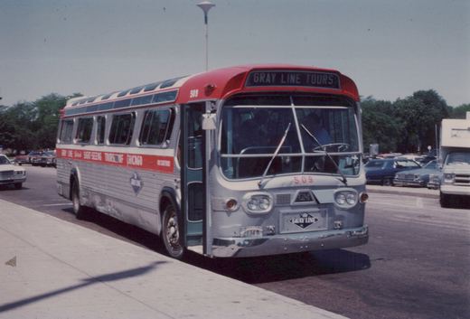 A silver and red Gray Line sightseeing bus, number 509, is parked on a city street with 1970s cars in the background.