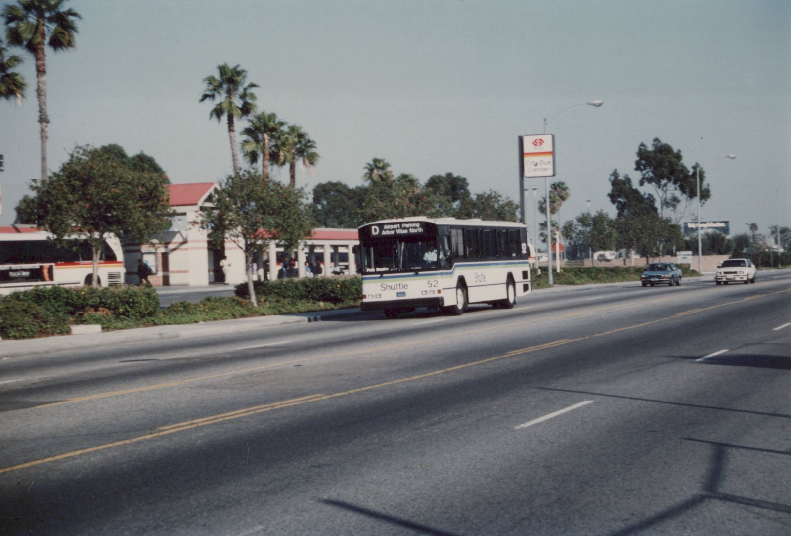 A white shuttle bus with the number 52 is driving on a street lined with palm trees. A sign for the City Bus Center is visible in the background.