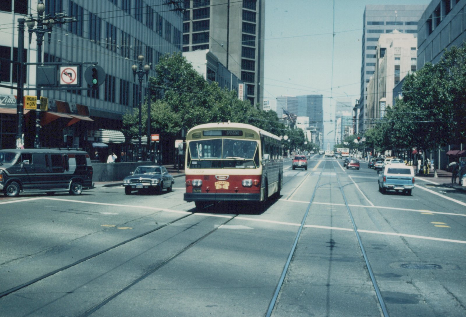 A red and cream trolleybus with the number 4009 on its front travels down a wide city street with visible trolley wires, surrounded by other cars and tall buildings on a sunny day.