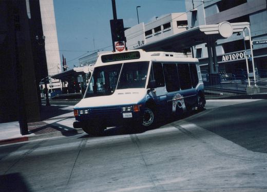 A blue and white motor bus with 'REIMBROCK' on the side and 'C DOWNTOWN' on the front sign is turning on a city street under a clear sky.