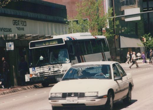 A white city bus with red and blue stripes is stopped on a street in Fort Worth, TX, near a building with signs for 'GREAT FOOD' and 'McKesson's'. Pedestrians cross the street and a white car is in the foreground.