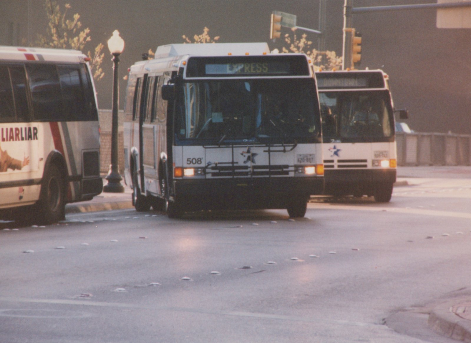 Two white buses with blue star emblems are on a city street; the lead bus displays 'EXPRESS' and the number 508, and the trailing bus shows 'DOWNTOWN'.