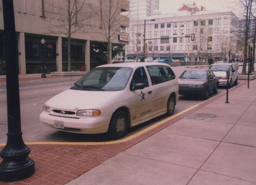 A white van with 'IMS OPERATIONS' lettering and the number 56 on its hood is parked on a city street, with other cars and buildings in the background.